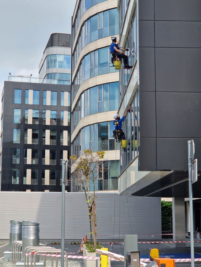 Two employees wash the windows of a tall office building in an urban setting.