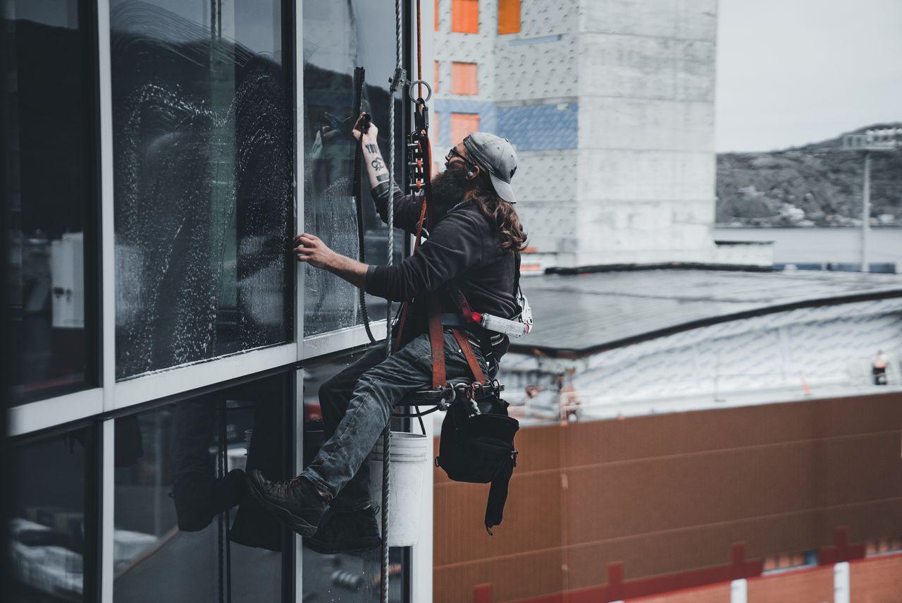 Un homme nettoyant les vitres d'un gratte-ciel avec un harnais, illustrant le travail en hauteur en milieu urbain.